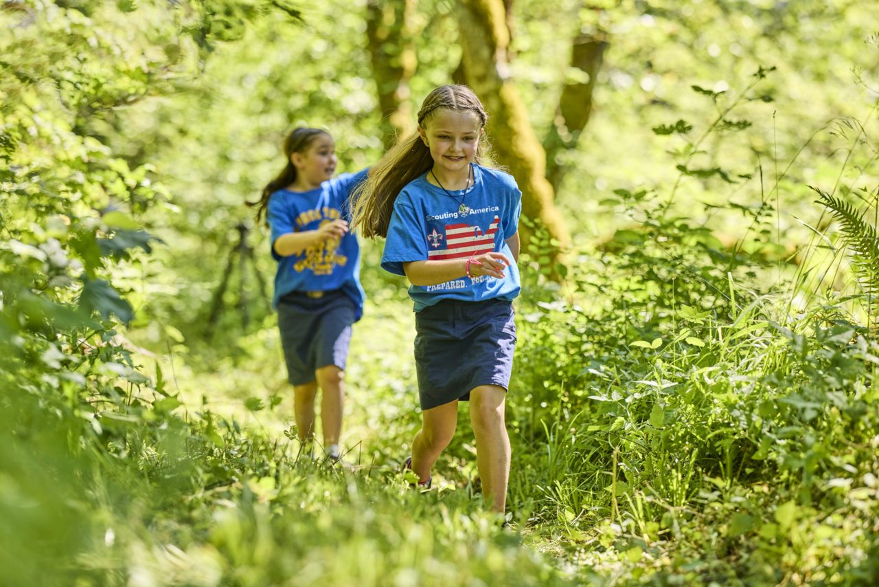 Two Cub Scouts running through green woods