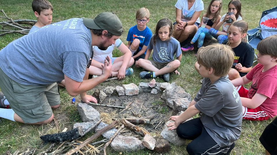 A leader showing Cub Scouts how to lay sticks inside a stone fire ring