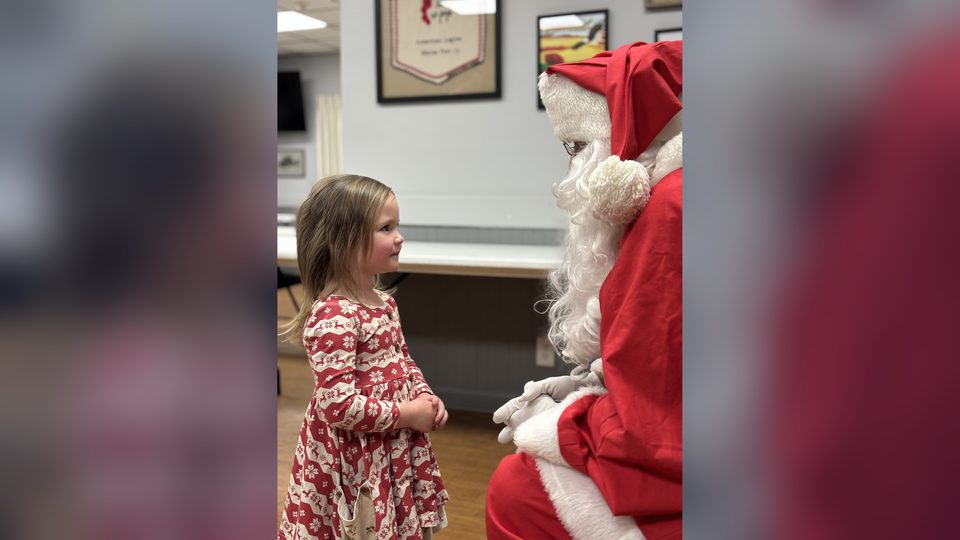A young girl in a red holiday dress talking with Santa