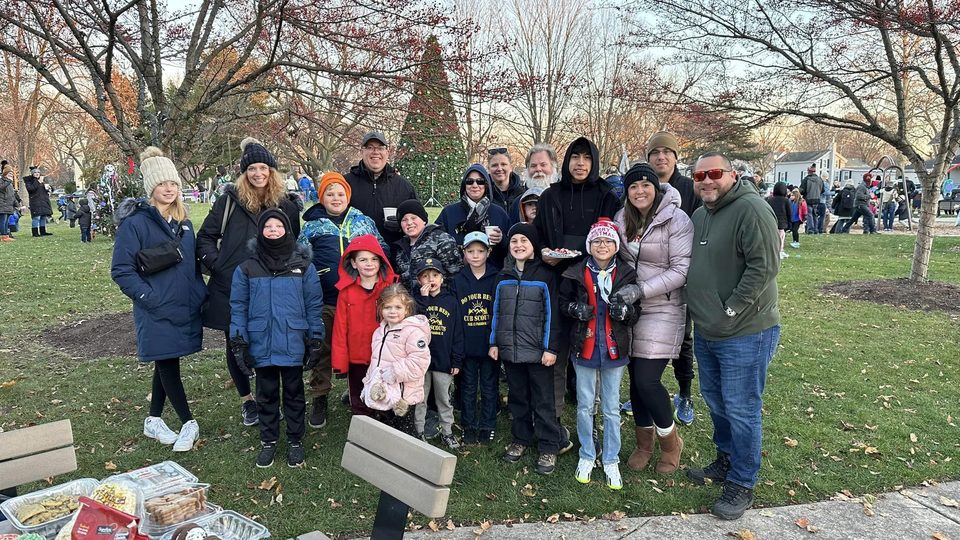 Pack families gathered in a park in front of a decorated holiday tree, with a table of cookies