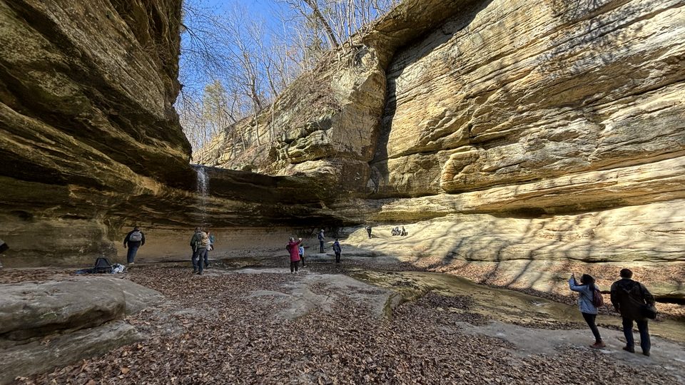 Hikers exploring a sandstone canyon with a small waterfall on a sunny winter day
